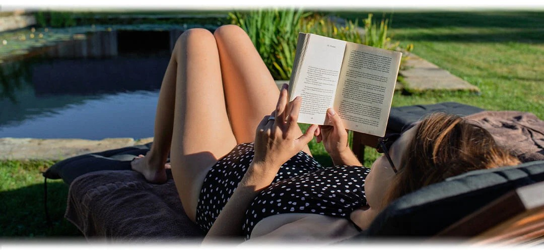 A woman reading a book in a sun lounger by a pond